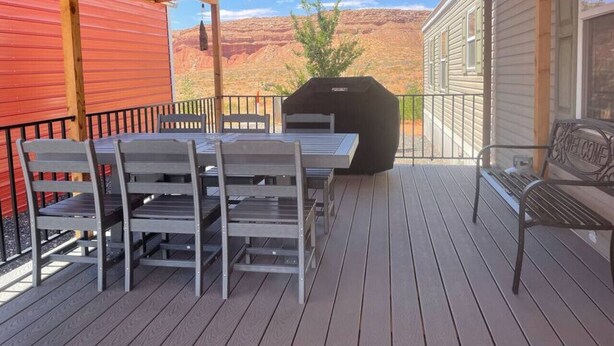 Een overdekt terras buiten met een tafel en stoelen, een barbecue en uitzicht op rode rotsformaties.