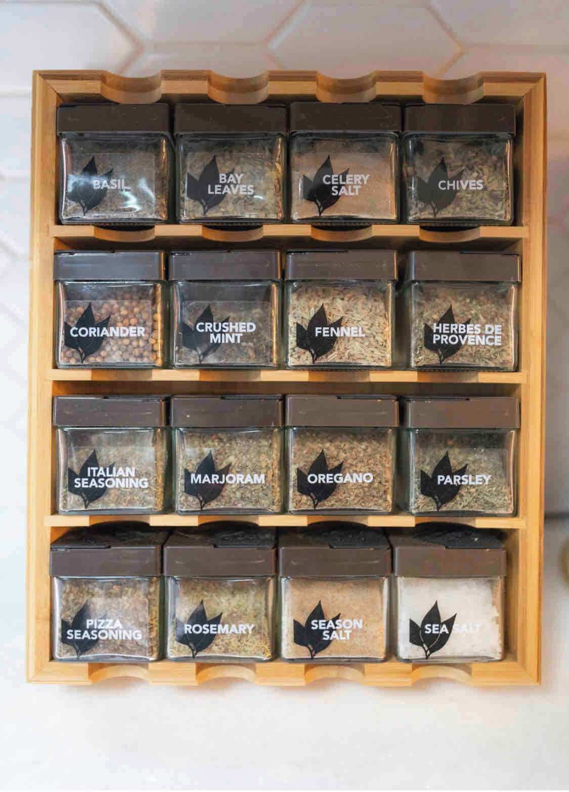 Un escurridor de madera con frascos de vidrio etiquetados que contienen diversas especias.