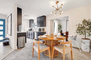 A modern kitchen with dark cabinets, a round dining table with chairs, and a ceiling light fixture.