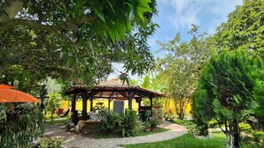 A gazebo with a tiled roof, surrounded by lush greenery and a stone pathway. - Amazing and comfortable country house. Very close to the Rozo small town. (Palmira Rozo)