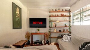 Una sala de estar con un televisor de pantalla plana montado en la pared, un sofá, una mesa de centro de madera y una estantería con objetos decorativos.