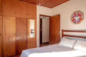 Quarto com guarda-roupa de madeira, cama com roupa de cama branca e um adorno na parede.