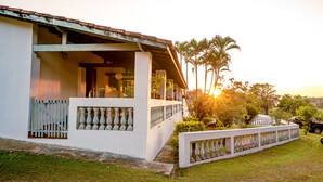 Un edificio blanco con balcón, rodeado de follaje y palmeras.