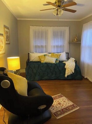 Una camera da letto con un letto, una ventola a soffitto, una lampada e una sedia.