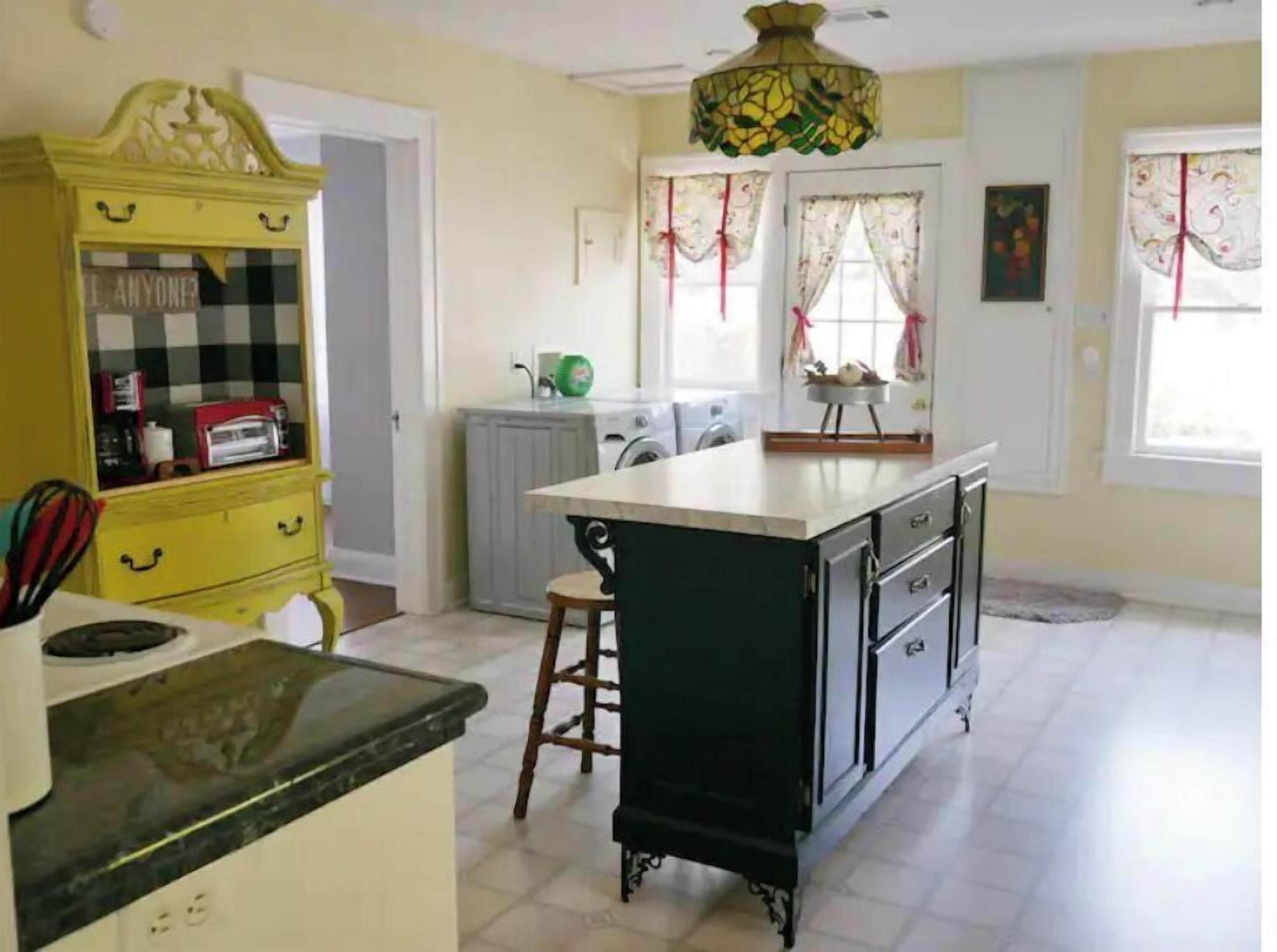 A kitchen with a central island, a yellow cabinet, and a chandelier.