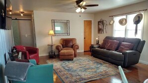 A living room with a brown leather sofa, a teal armchair, a red armchair, a patterned rug, and a ceiling fan. - Rambler *pet friendly* garage private deck (Amarillo)