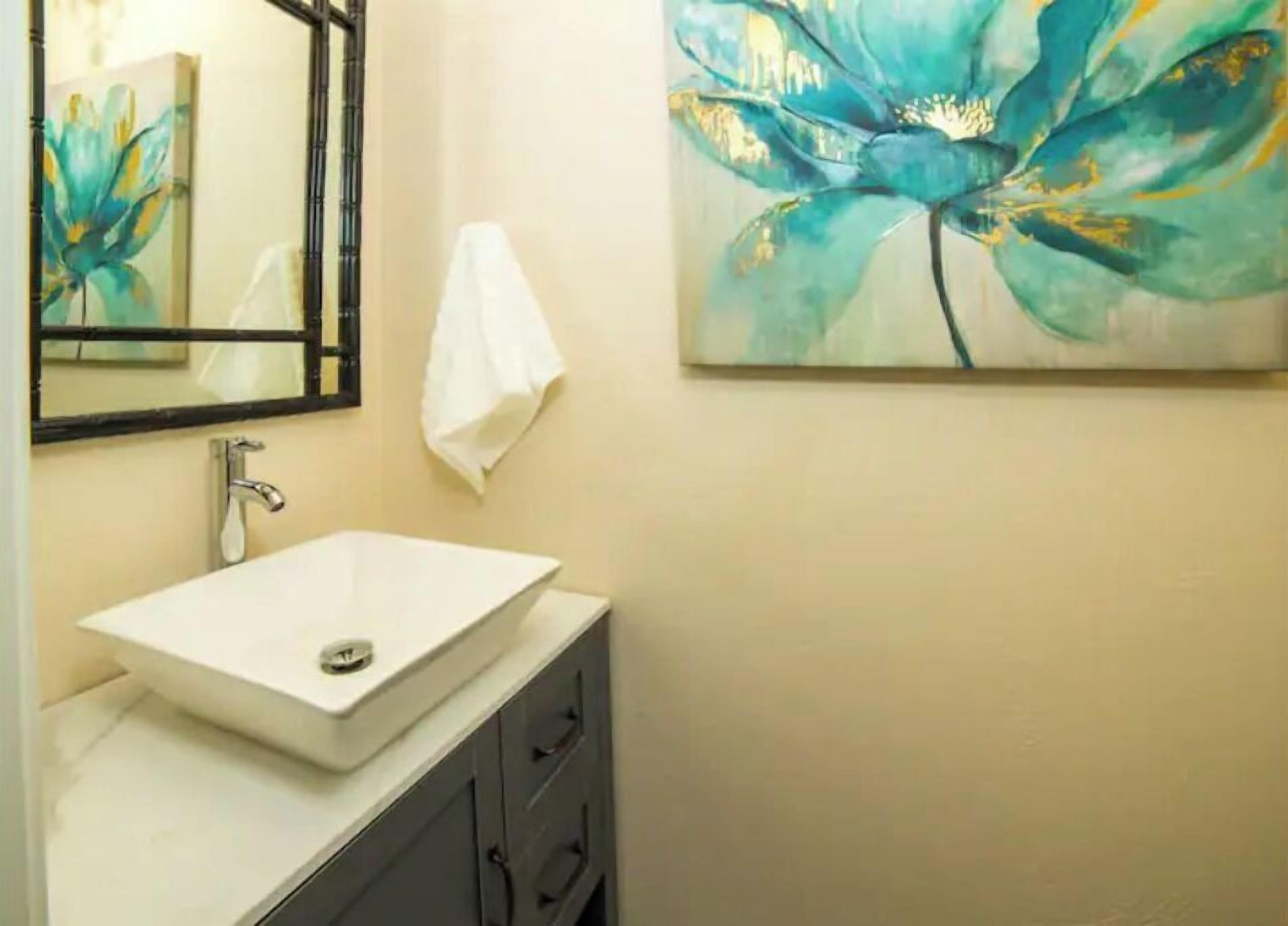 A bathroom with a white sink, a mirror, and a painting of blue flowers on the wall.