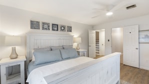 Une chambre à coucher avec un lit, des tables de chevet, un ventilateur de plafond et des œuvres d’art accrochées au mur.