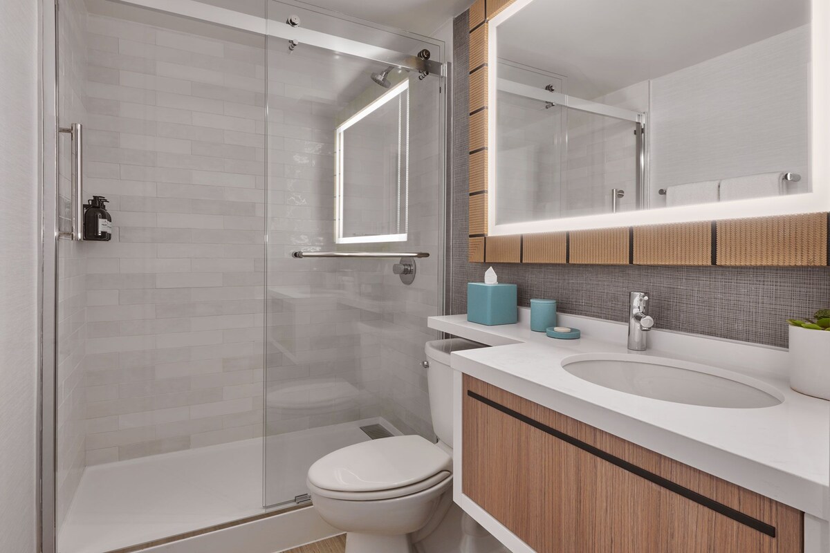 A modern bathroom with a glass shower enclosure, a white toilet, a sink with a mirror above, and wooden cabinetry.