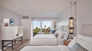 Een hotelkamer met twee bedden, een bureau, een lamp en uitzicht op palmbomen.