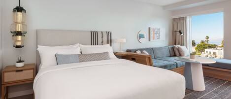 A modern hotel room with a large bed, a sofa, a small table, and a view of the city.
