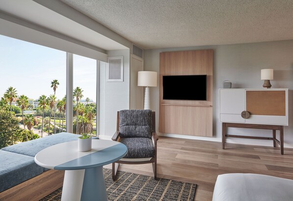 Una habitación de hotel moderna con un ventanal grande, un televisor de pantalla plana, una zona de estar con una mesa y un mueble pequeño.