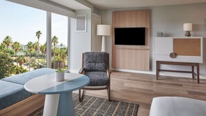 Een moderne hotelkamer met een groot raam, een flatscreen televisie, een zithoek met een tafel en een klein kastje.