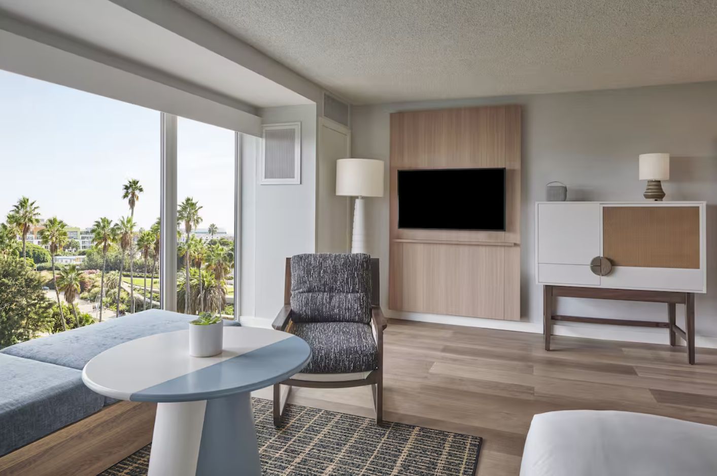 Ein modernes Hotelzimmer mit großem Fenster, einem Flachbildfernseher, einem Sofa, einem Sessel und einem kleinen Tisch.