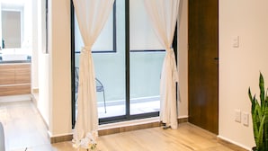 A modern room with a large window, a round glass table with a plant, a wicker chair, and a wooden door. - Noma Condesa Mexico City by Lumina (Mexico City)