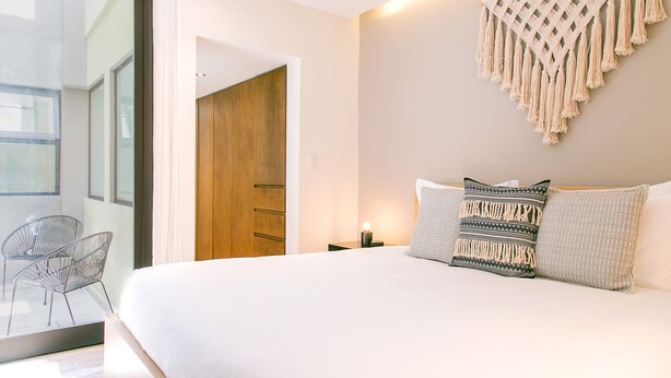 A modern bedroom with a large bed, a macrame wall hanging, and a view of a wooden door. - Noma Condesa Mexico City by Lumina (Mexico City)