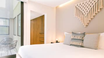 Un dormitorio moderno con una cama grande, un colgador de macramé en la pared y vistas a una puerta de madera.