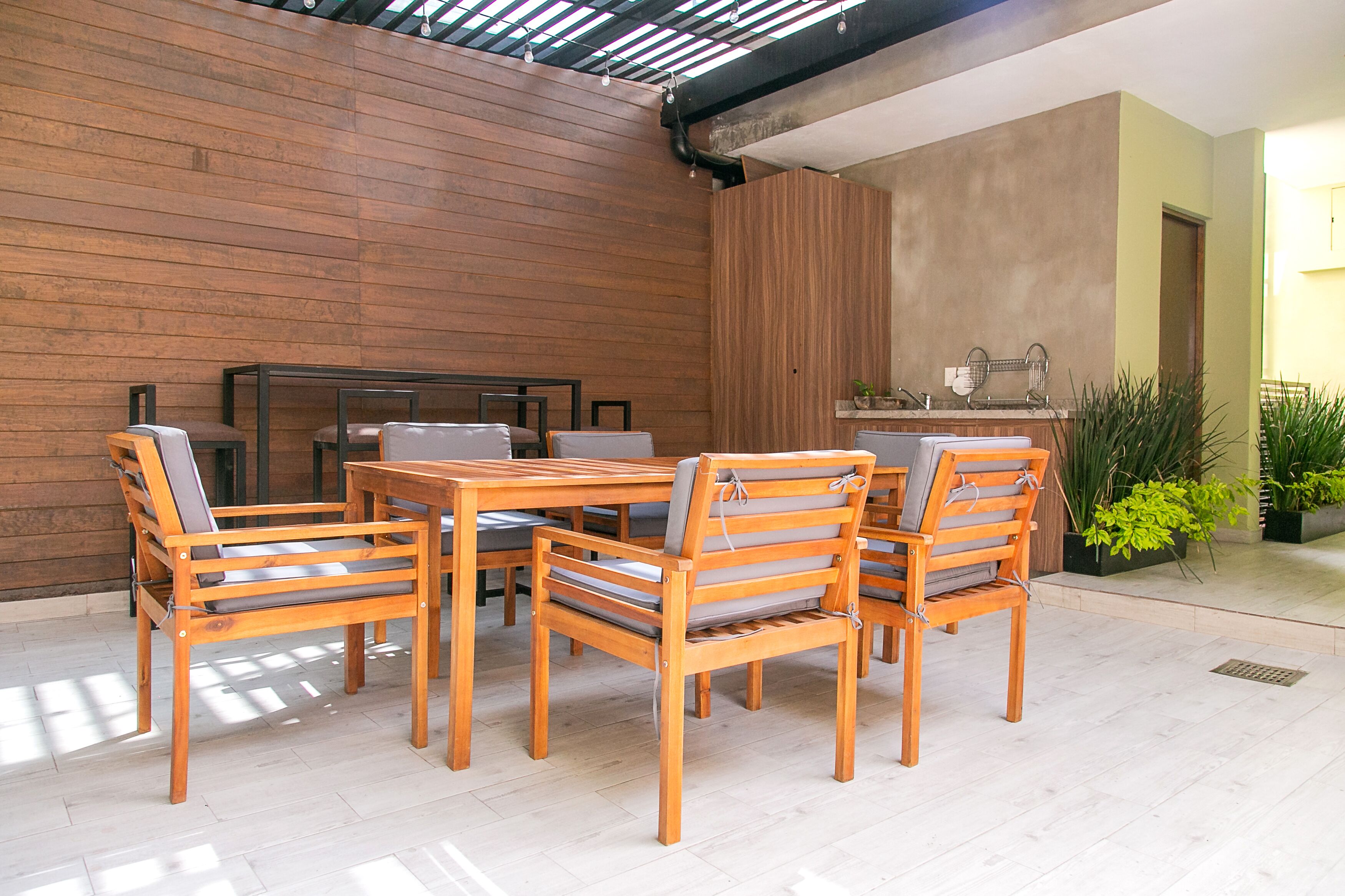 Una mesa de comedor de madera con seis sillas, una zona de cocina con un lavamanos y encimera, y una pared de madera.