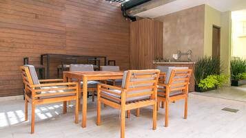 Una mesa de comedor de madera con seis sillas, una zona de cocina con un lavamanos y encimera, y una pared de madera.