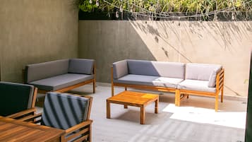 Un patio con mobiliario de madera, incluyendo sofás y una mesa, y una guirnalda de luces.