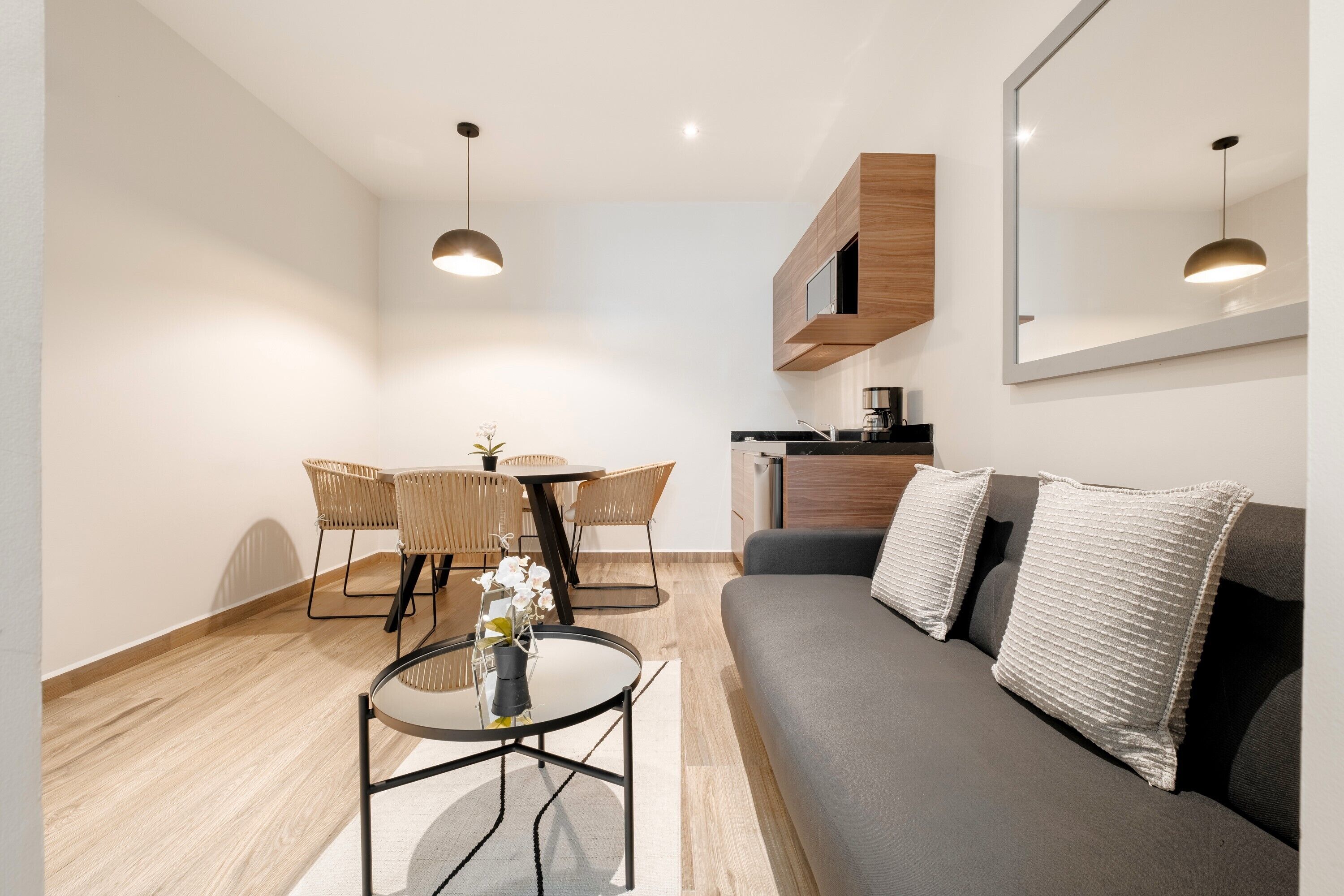 Una sala moderna con un sofá gris, una mesa redonda, sillas de mimbre y una mesa de comedor.