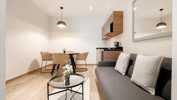 Una sala moderna con un sofá gris, una mesa redonda, sillas de mimbre y una mesa de comedor.