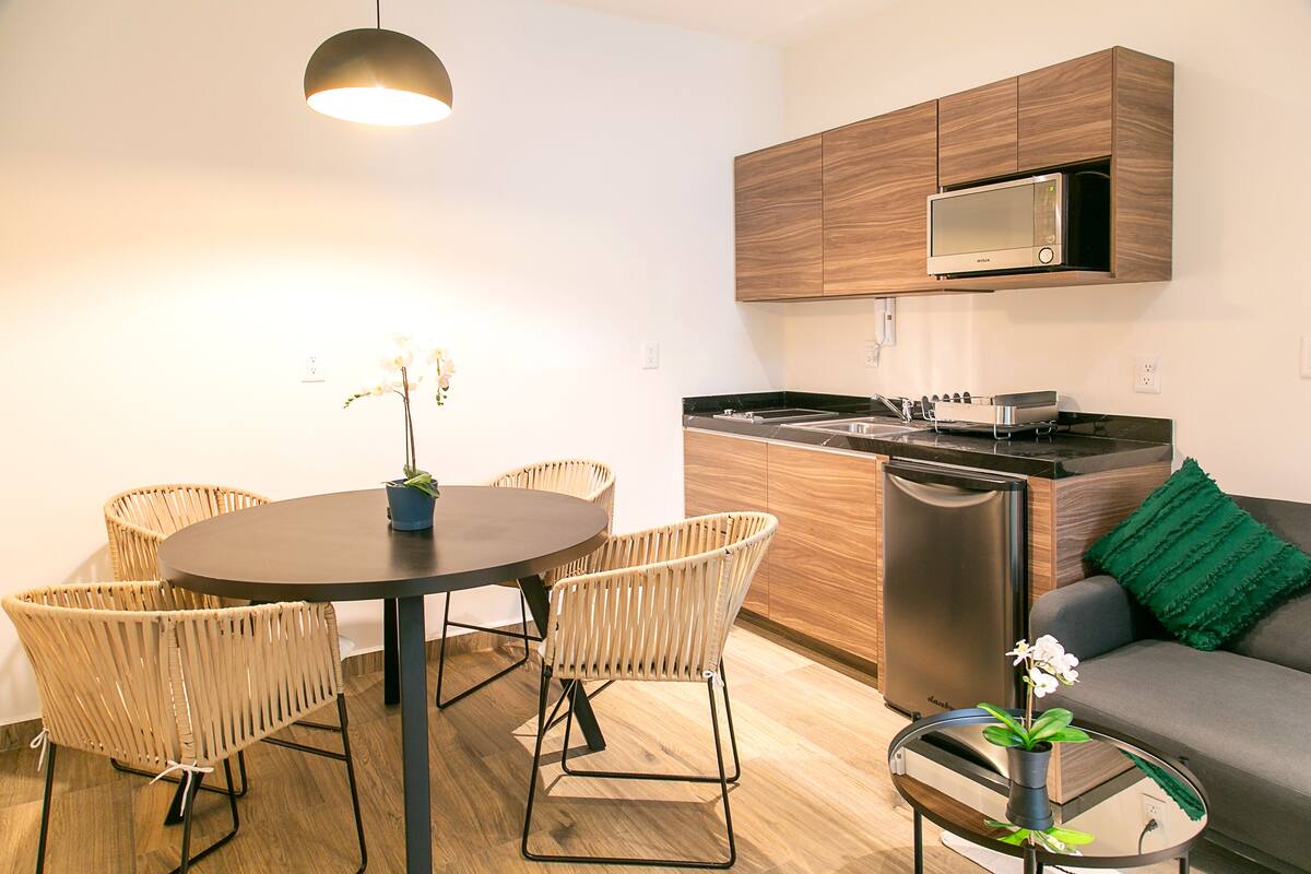 Eine moderne Küche mit eingebauten Geräten, ein Essbereich mit Korbstühlen und ein Sofa mit einem gr ünen Kissen.