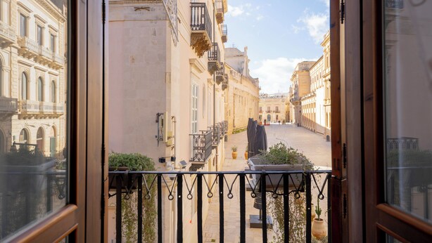 A view from a balcony overlooking a narrow street with buildings on either side.