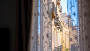 A view through a window with ornate iron railings, showcasing a building with balconies and a clear sky.