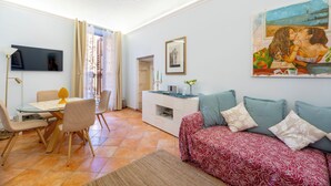 A living room with a sofa, a dining table, and a TV mounted on the wall.