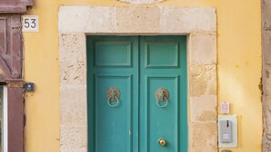 A turquoise double door with a decorative metal grille above it, set in a yellow building with a stone base.