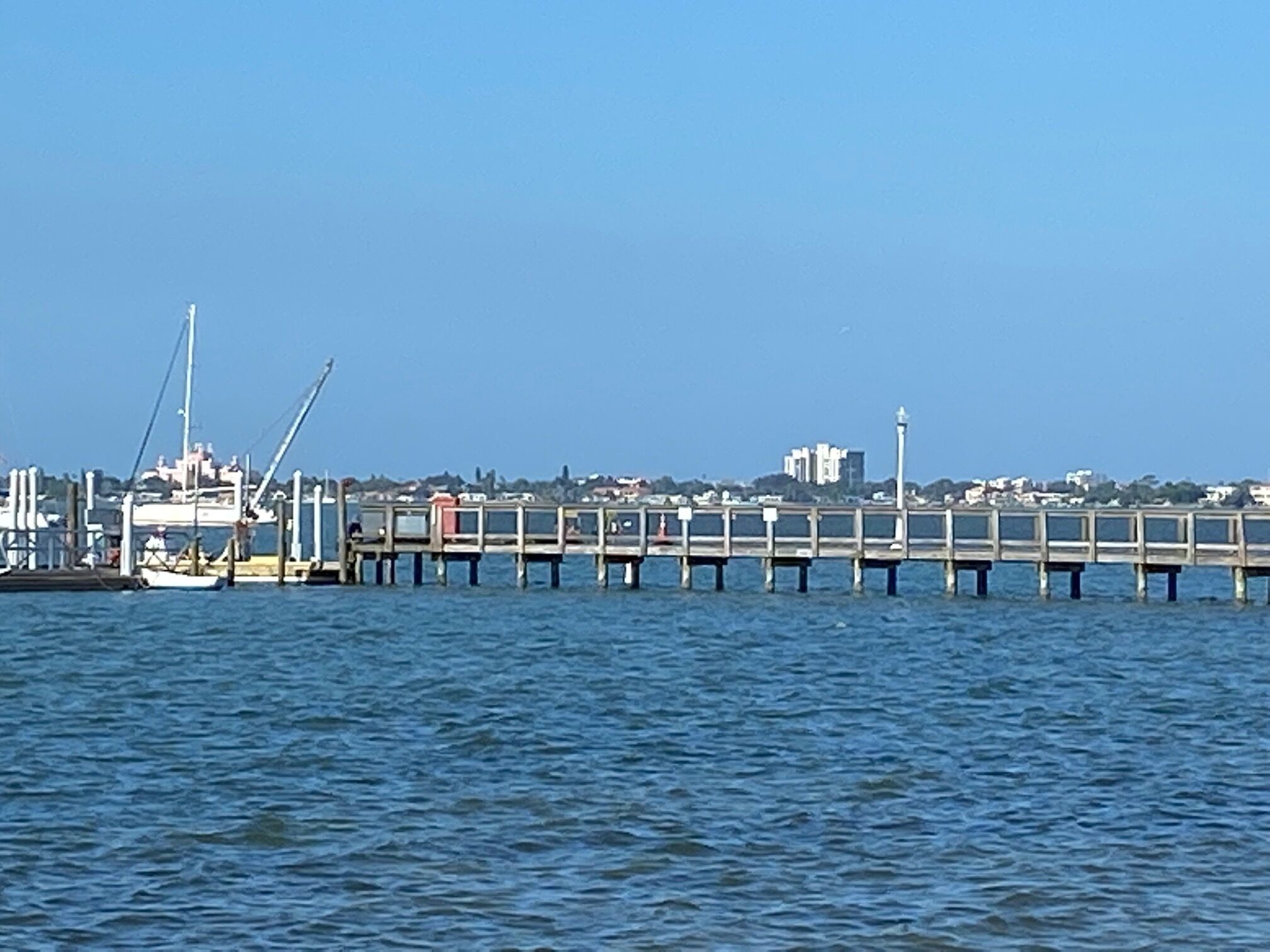 A pier extending into calm waters with a cityscape in the background.