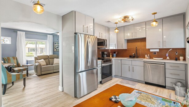 A modern kitchen with stainless steel appliances, grey cabinets, and a wooden dining table. - Waterfront Marina District  Luxury Home & In-law Suite (Gulfport)