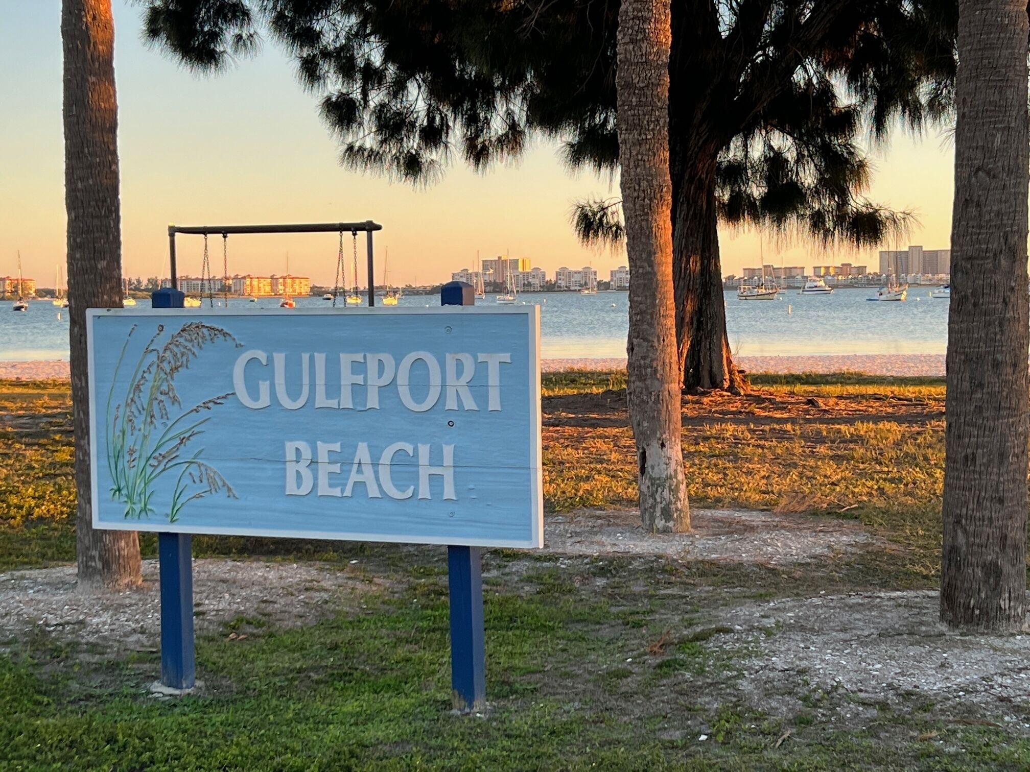 A sign for Gulfport Beach with a view of the beach and water in the background.