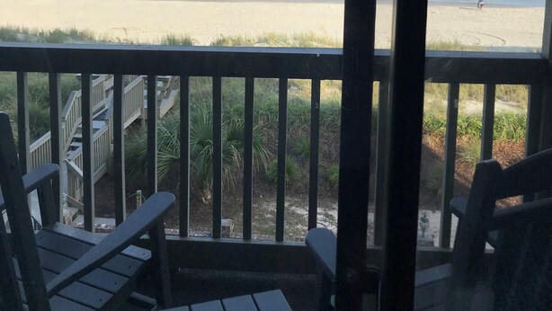 A beach view from a covered deck with wooden chairs and a table.
