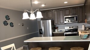 A modern kitchen with dark cabinets, stainless steel appliances, and a central island with stools.