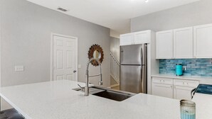 A modern kitchen with white cabinetry, a stainless steel refrigerator, a blue kettle, and a unique wall-mounted faucet. - 3bd/3bth, Private Pool & View, 5mi to Disney Parks (Kissimmee)