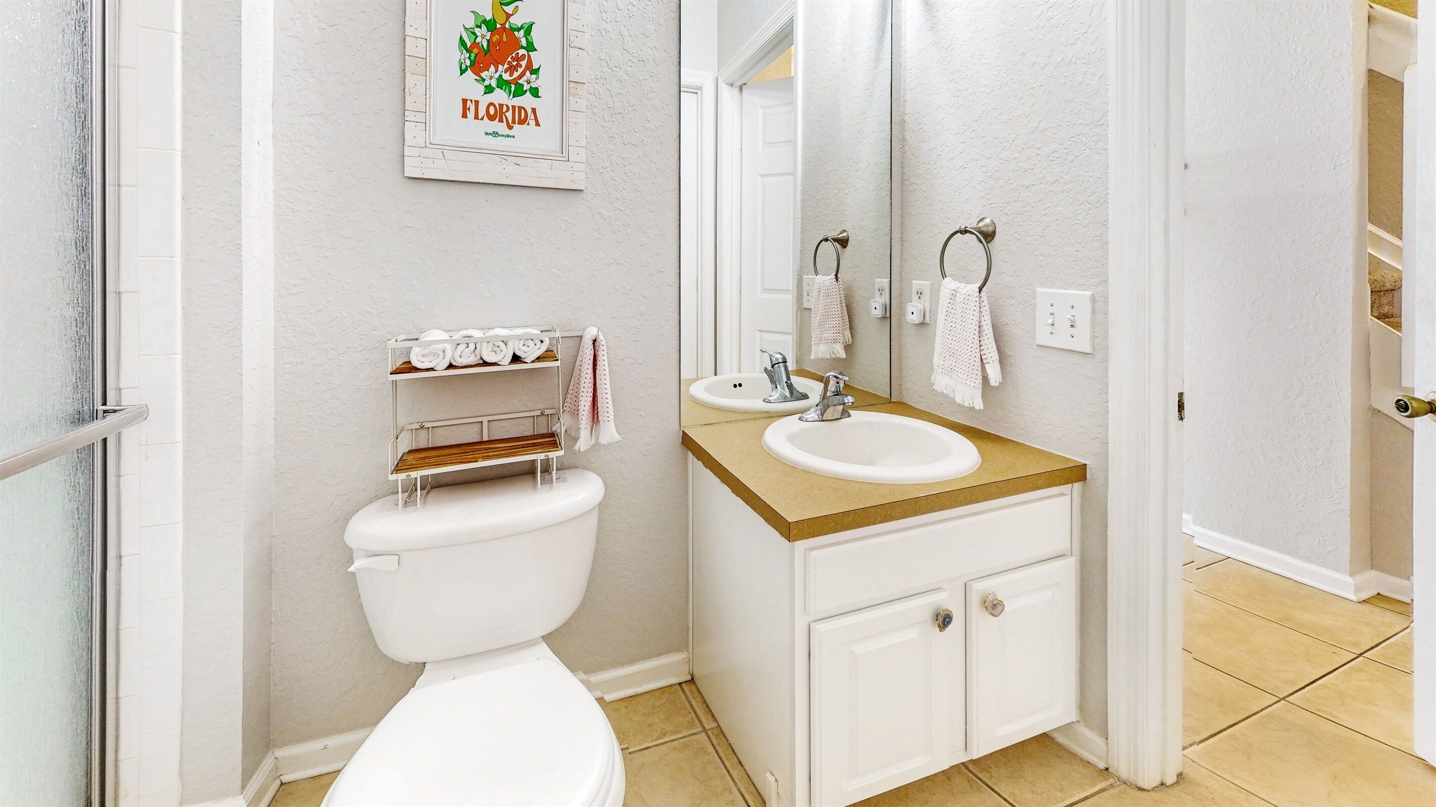 Un baño con inodoro, lavamanos y un mueble. Hay un perchero con toallas y un cuadro en la pared.