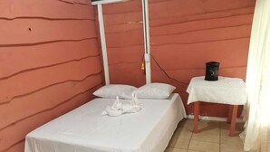 A small, single-bed room with a white bedspread, two pillows, a small table with a black object on it, and a red wall. - Millar de Aves Eco Cabin with mountain views and trails (Cerro Alto)