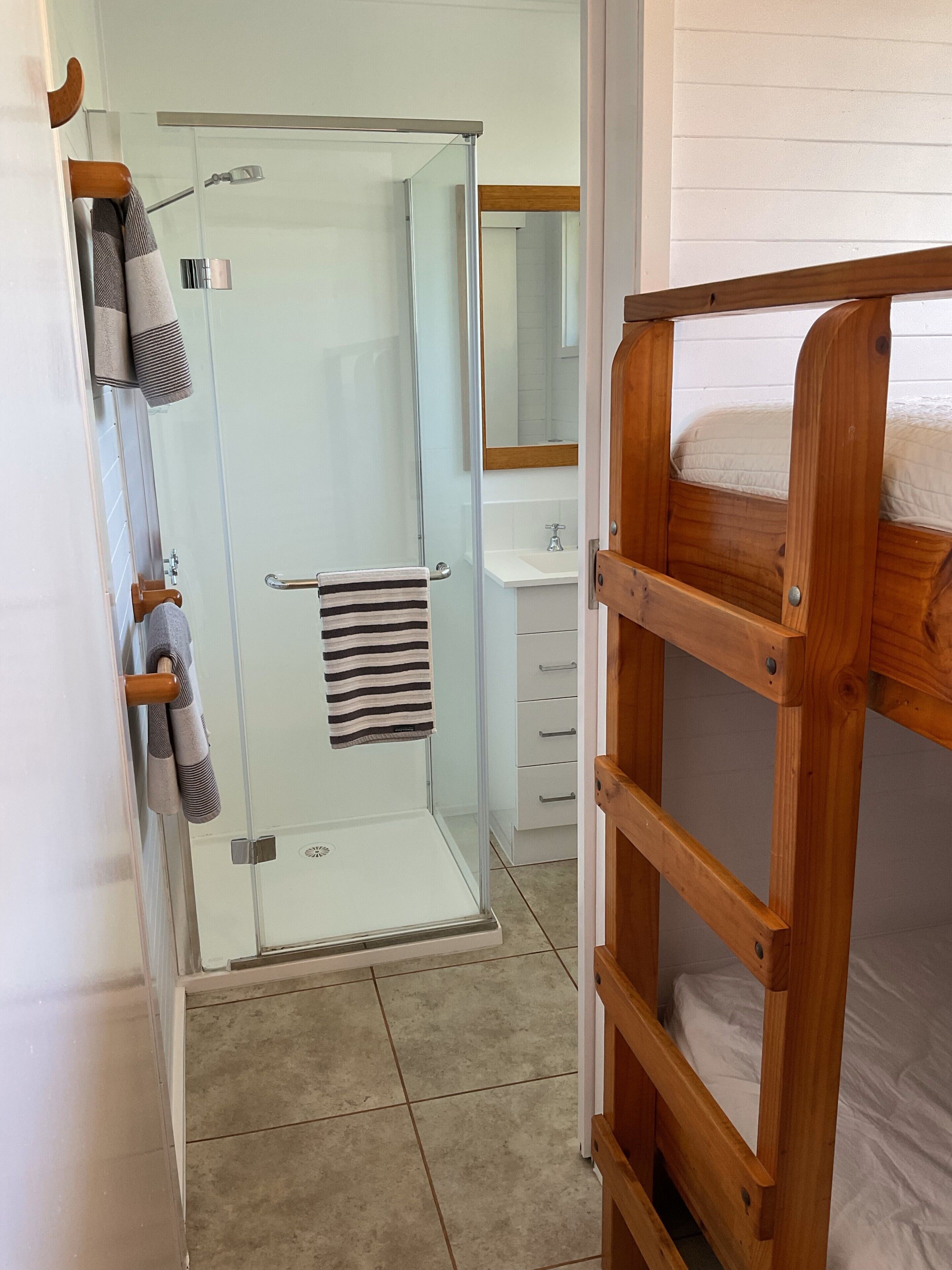 Une salle de bain avec une douche à parois de verre, un lit superposé en bois et un lavabo blanc.