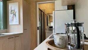 A modern kitchen with wooden cabinets, a white countertop, a coffee maker, and a framed artwork on the wall. - Marlo Hideaway (Marlo)