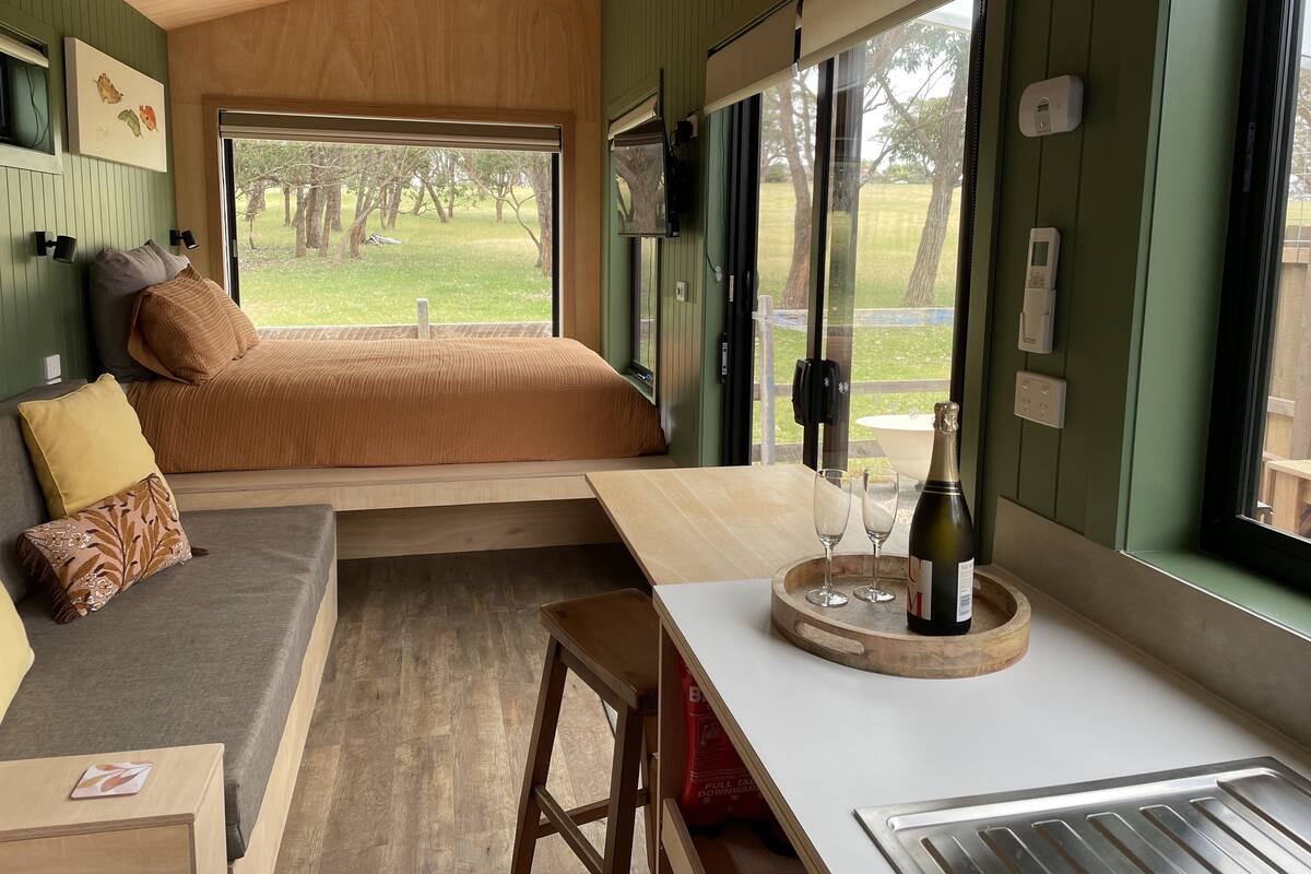 Une pièce confortable avec un lit, une petite table avec des verres et une bouteille, un banc et une vue sur un espace verdoyant.