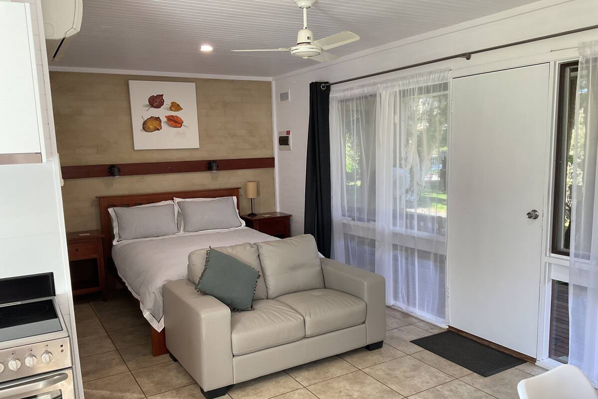 Une chambre d’hôtel comprenant un lit, un canapé, un ventilateur de plafond, une fenêtre avec des rideaux et une vue sur l’extérieur.