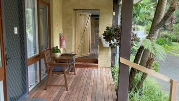 A wooden deck with a table and chairs, a door marked "Staff Only," and a view of a garden with plants and a palm tree.