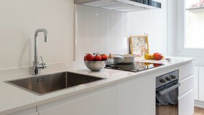Cozinha moderna com pia de aço inoxidável, forno embutido e bancada branca.