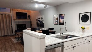 A modern kitchen with a dishwasher, a sink, and a dining area with chairs and a table.