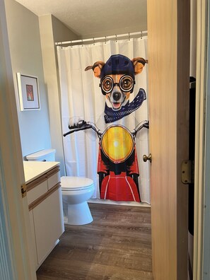 Bathroom features a unique shower curtain with a cartoon dog design, a toilet, a cabinet, and a framed picture on the wall.