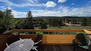 A wooden deck with a round table and two chairs, overlooking a scenic landscape with hills and trees.