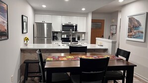 A modern kitchen with white cabinets, stainless steel appliances, and a dining area with a wooden table and chairs.