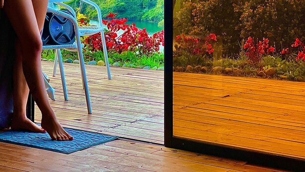 A woman in a bikini standing by a glass door with a view of a mountainous landscape and a body of water. - Hotel Selva Negra (Guatapé)